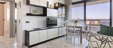 A modern kitchen with white cabinets, a dining area with a table and chairs, and a large window offering a view.