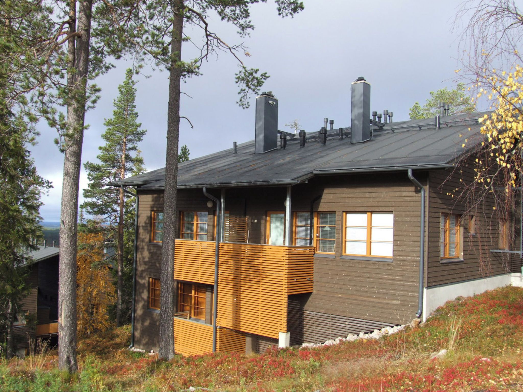Une maison moderne à deux étages, dotée d’un toit en pente, de grandes fenêtres et d’un balcon en bois.