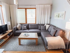 Una sala de estar con un sofá gris, una mesa de centro, un televisor y una ventana con persianas.