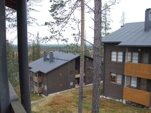 A multi-story building with a flat roof, surrounded by trees and a view of a distant landscape.