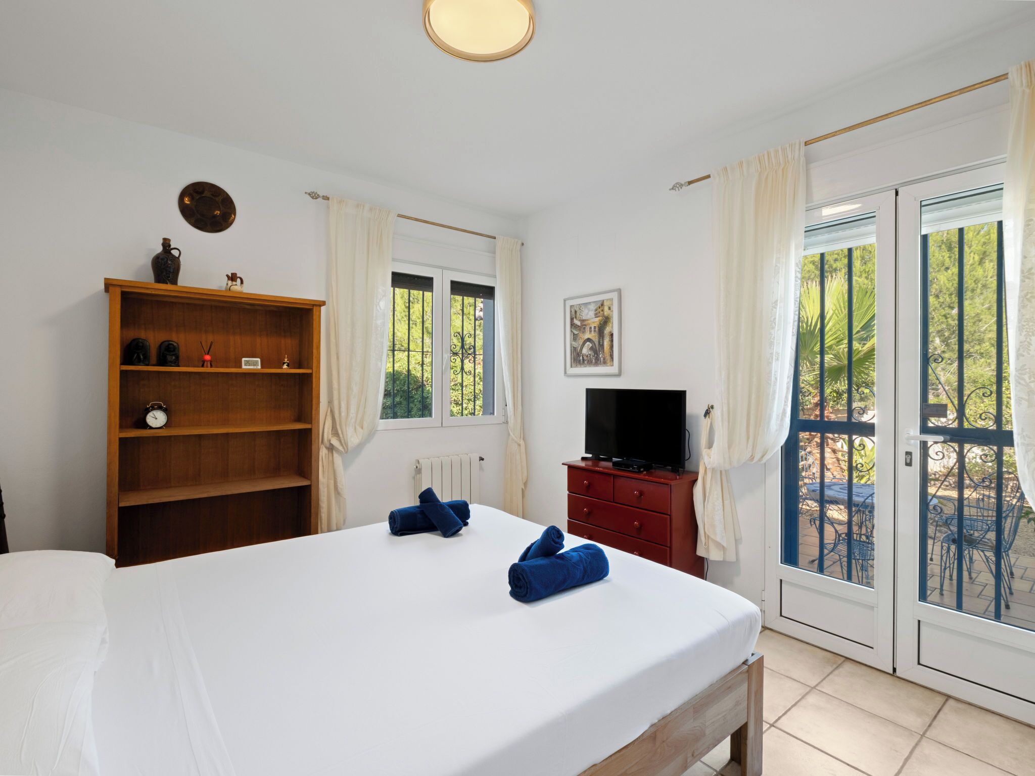 A bedroom with a bed, a TV, a wooden shelf, a window, and a painting.