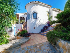 Un bâtiment blanc agrémenté de touches de bleu, avec un escalier et une végétation luxuriante tout autour.