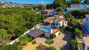 Une villa avec piscine, entourée d’une végétation luxuriante et adossée à des collines.