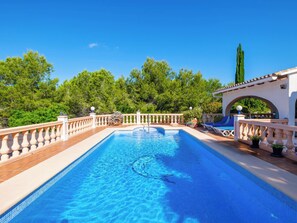 Une piscine dotée d’une terrasse carrelée, d’un toboggan et d’une pergola offrant une vue sur les arbres.