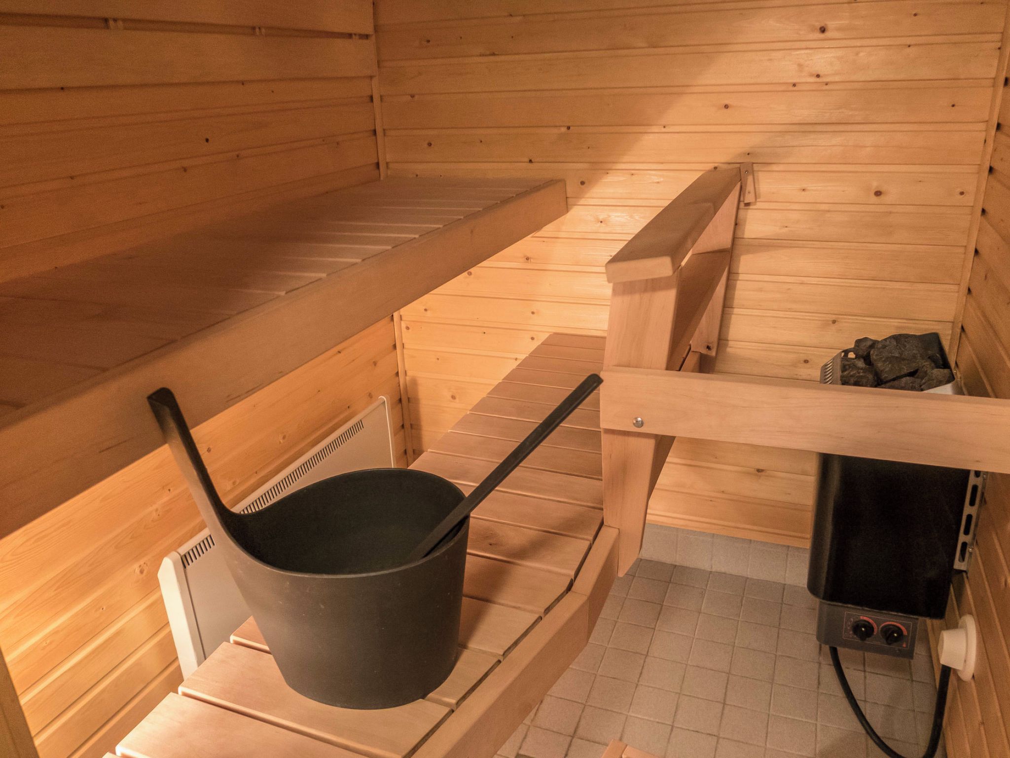 Una sala de sauna con un banco de madera, una tina de sauna negra y un calentador de sauna en el suelo.