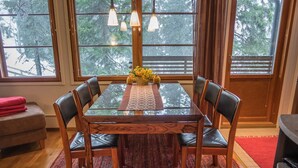 Une salle à manger avec une table en verre, six chaises, un tapis rouge et une vue sur les arbres à travers de grandes fenêtres.