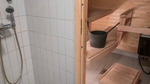Une salle de bain rustique, avec des murs en bois, comprenant une douche, une étagère en bois avec un pot et une petite table en bois.