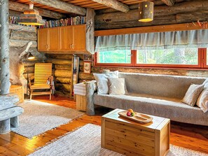 A cozy log cabin interior with a sofa, wooden coffee table, and a bookshelf filled with books.