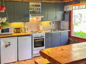 A compact kitchen with a microwave, toaster, coffee maker, and a stove. There are cabinets above the counter and a window with a view of greenery.