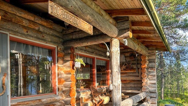 Une cabane en rondins avec une véranda, des meubles en bois et des plantes suspendues.