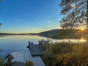 A wooden dock extending into calm water with a clear sky and a sunset in the background.