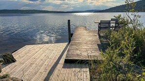 Une jetée en bois s’étendant sur un lac paisible, avec un banc et une petite table, le tout entouré de verdure et d’un paysage boisé.