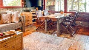 L’intérieur d’un chalet rustique est aménagé avec une table à manger en bois, des chaises, un canapé et un téléviseur.