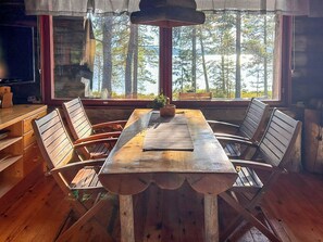 A wooden dining table with chairs, a television, and a window with a view of trees.
