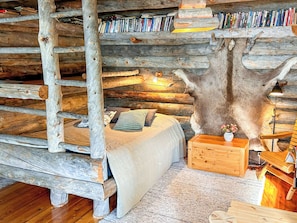 A log cabin interior with a bed, a wooden chest, a lamp, and a bookshelf filled with books. - Nanguvilla by Interhome (Inari)
