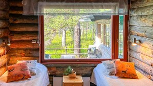Une chambre située dans un chalet en rondins, avec deux lits, une petite table et une fenêtre donnant sur la forêt.