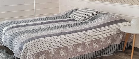 Un dormitorio con una cama, una silla y una pared blanca con una lámpara colgante.