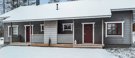 A two-story house with a snow-covered roof, a front porch with a bench, and a chimney.