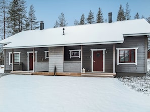 Une maison à deux étages, dont le toit est recouvert de neige, avec une véranda à l’avant, ornée d’un banc, et une cheminée.