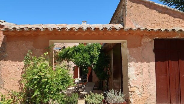 A rustic building with a tiled roof, a wooden door, and a small garden area with potted plants. - Les Huppes by Interhome (Saint Saturnin d'Apt)