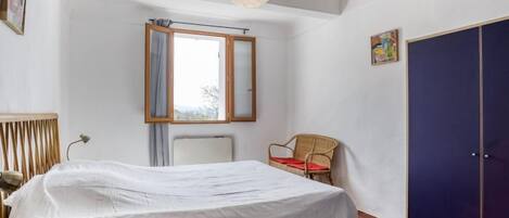 Een slaapkamer met een bed, een stoel, een kledingkast en een raam met uitzicht op het landschap.