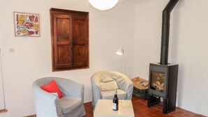 A living room with a sofa, a small table with a bottle and glass, a wooden cabinet, a fireplace, and a wall-mounted artwork. - Les Huppes by Interhome (Saint Saturnin d'Apt)