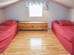 Una habitación con dos camas, un banco de madera, una ventana con cortinas y una lámpara fijada a la pared.