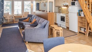 A cozy living room with a grey sofa, wooden dining table, and a kitchen area with white appliances. - Nelikko b by Interhome (Kuusamo)