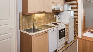 A compact kitchen with wooden cabinets, a stainless steel sink, a stove, and a microwave. - Nelikko b by Interhome (Kuusamo)
