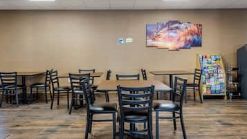 A restaurant with a long wooden table and chairs, a wall-mounted painting, and a menu board.