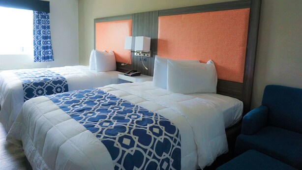 A hotel room with two beds, a nightstand, a chair, and a window with curtains.