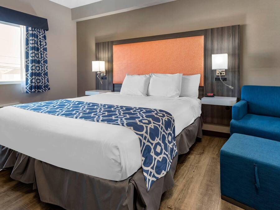 Habitación de hotel con una cama grande, dos mesitas de noche con lámparas, un sillón azul y vistas al exterior a través de una ventana con cortinas estampadas.