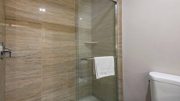 A glass-enclosed shower with a white towel hanging on a rack, a toilet, and a marble-patterned wall.