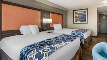 A hotel room with two beds, a nightstand, a lamp, and a painting on the wall.