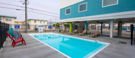 A swimming pool area with lounge chairs and a building with a blue and white facade.