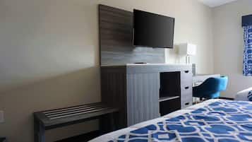A hotel room with a bed, a desk with a flat-screen TV, a chair, and a lamp.