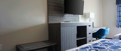 A hotel room with a bed, a desk with a flat-screen TV, a chair, and a lamp.