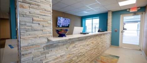 A reception area with a stone wall, a flat-screen TV, a bowl-shaped vase, and a door with an exit sign.