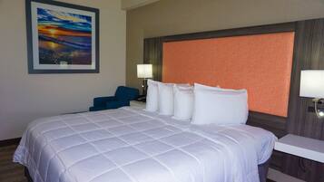Une chambre d’hôtel avec un grand lit, une tête de lit ornée d’un panneau orange texturé, un tableau encadré au mur, une chaise bleue et une table de chevet avec une lampe.