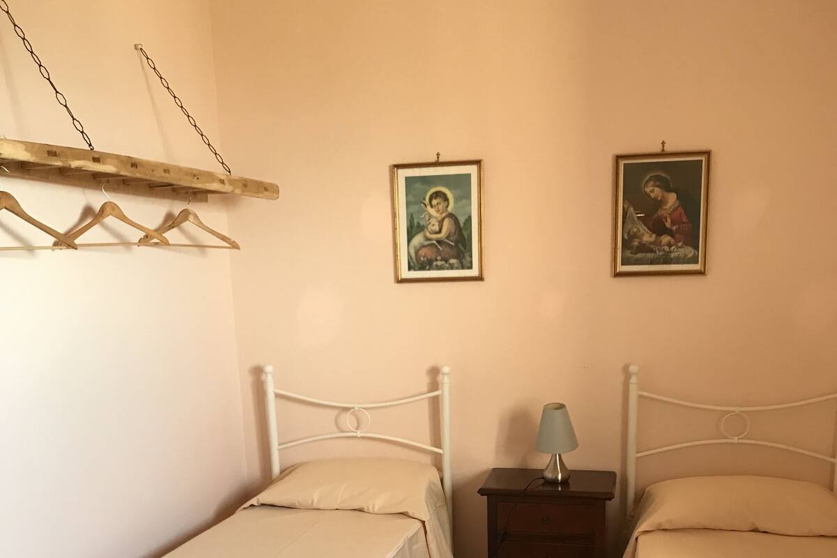 Un dormitorio con dos camas individuales, una mesita de noche, una lámpara y dos cuadros en la pared.