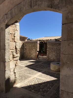 Un corredor de piedra con arco y suelo de baldosas que conduce a un edificio con tejado de tejas.