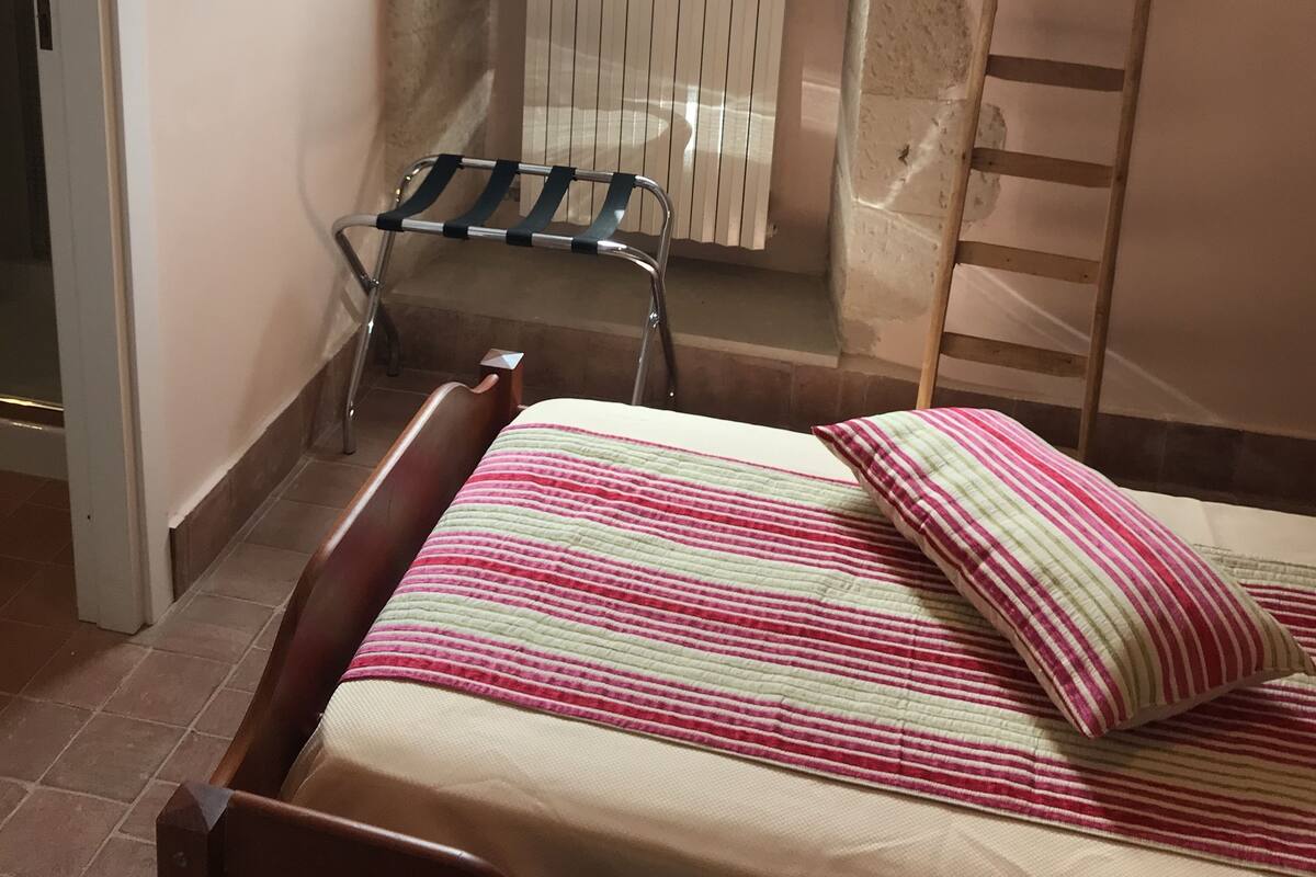 Una habitación pequeña con cama, un radiador, una ventana y una escalera.