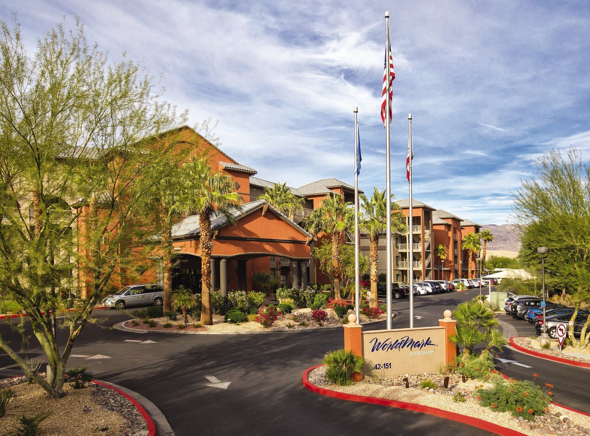 Een hotelingang met een bord, Amerikaanse vlaggen en een parkeerplaats.