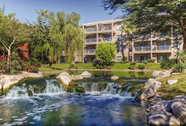 A multi-story hotel with balconies, a landscaped garden, and a small waterfall.
