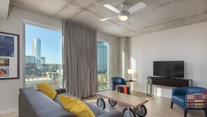A modern living room with a grey sofa, a wooden coffee table with wheels, a blue armchair, and a flat-screen TV on a stand. - DOWNTOWN Austin with ROOFTOP Pool and BBQ Area, Fire Pit & a Fitness Center (Austin)