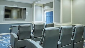 Une salle de conférence avec des fauteuils en cuir gris, un grand téléviseur à écran plat et une porte bleue en arrière-plan.