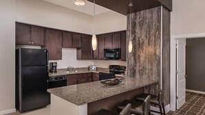 Eine moderne Küche mit dunklen Holzschränken, einer Granit Arbeitsplatte, einem schwarzen Kühlschrank, einer Mikrowelle, einem Herd und einer Bar mit zwei Barhocker.
