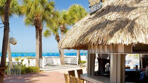 Un bar sulla spiaggia con tetto di paglia, palme e vista sull'oceano.