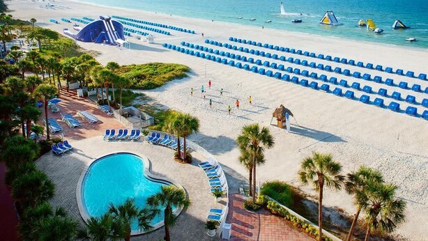 Un resort sulla spiaggia con piscina, lettini e vista sull'oceano.