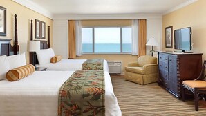 Ein Hotelzimmer mit zwei Betten, einem Sessel, einem Schminktisch und einem Fernseher.
